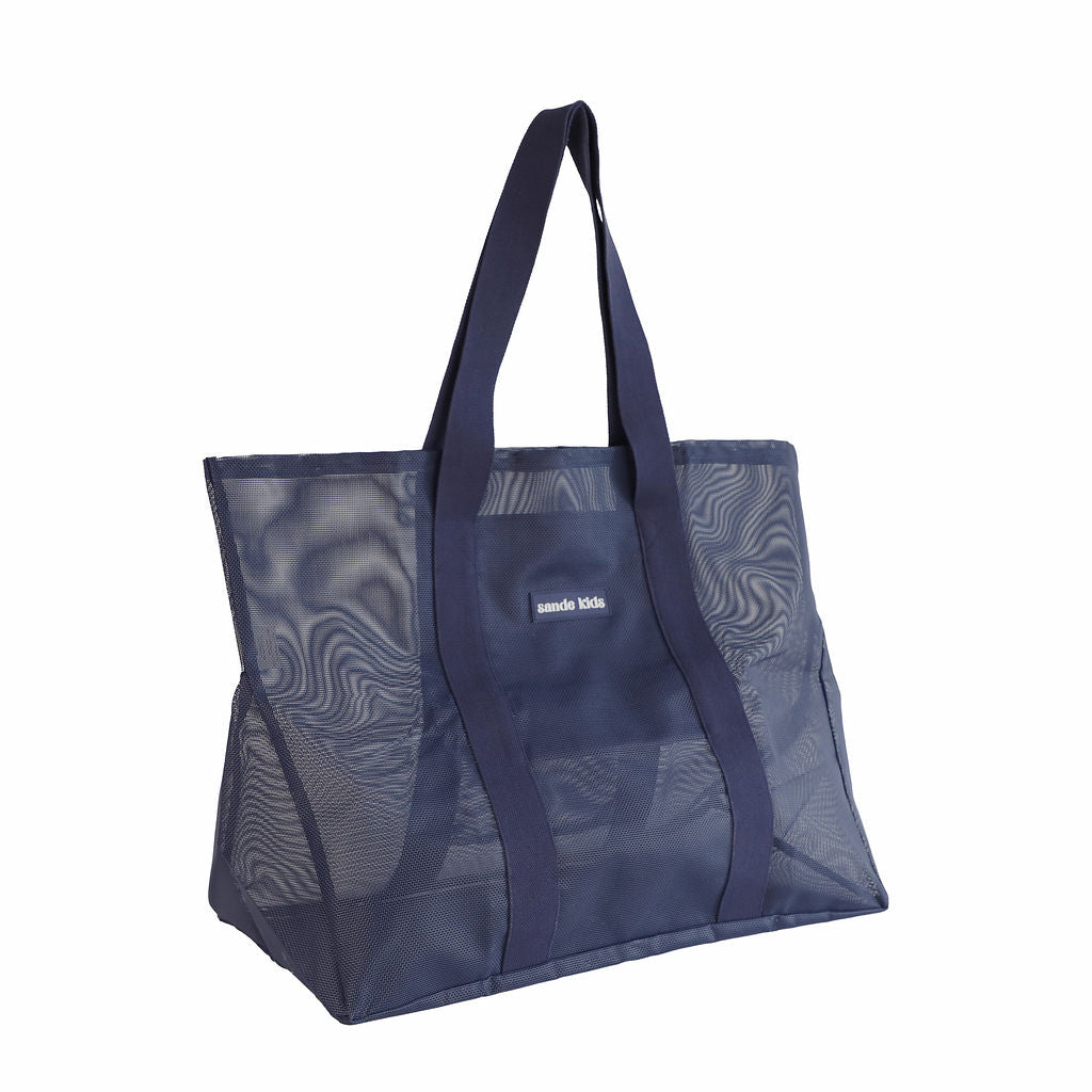 Oversized Sande Kids Beach Hauler mesh beach bag in Deep Sea Navy, displayed in a studio setting. Positioned at a 45° angle to highlight the mesh detail, thick cotton straps, and silicone Sande Kids logo. Set against a white background.