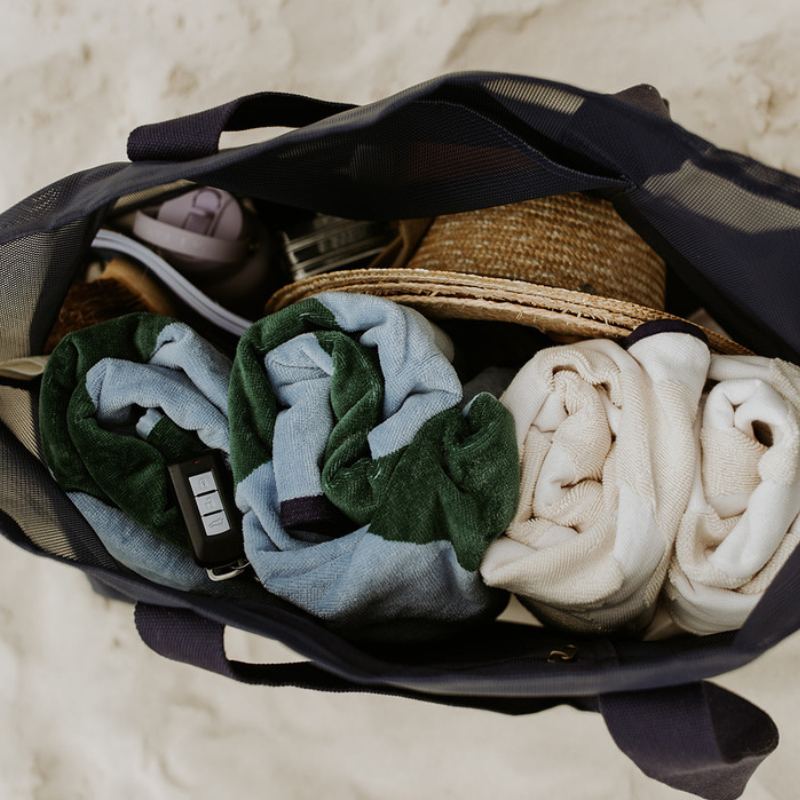Top view of the Sande Kids Beach Hauler mesh beach bag in Deep Sea Navy sitting on the sand. This image demonstrates the spacious capacity of the oversized mesh beach bag, showing how it can easily fit beach towels, hats, sunscreen, snacks, water bottles, and valuables.