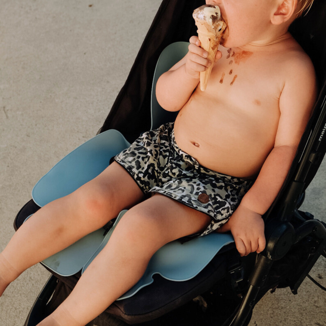 A little boy is sitting in a stroller on his Sande Kids™ waterproof car seat and pram liner, made of 100% food-grade silicone, ensuring safety and comfort. The little boy is enjoying dripping ice cream while his pram is protected from messes.