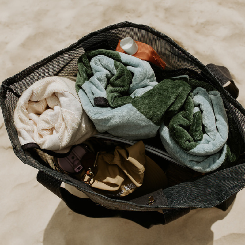 Top view of the Sande Kids Beach Hauler - Mini, a large mesh beach bag in Deep Sea Navy resting on the sand. This image highlights the large capacity of the  mesh beach bag, showcasing its ability to fit beach towels, hats, sunscreen, snacks, water bottles, and valuables—making it the perfect beach bag for all your essentials.