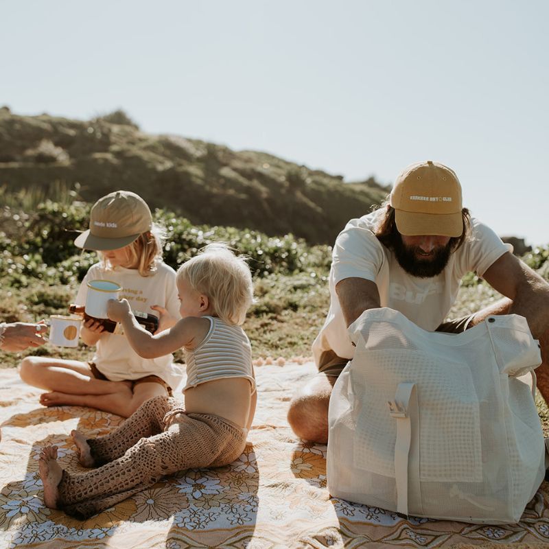 Dad and kids enjoying a picnic at Cabarita Headland, with dad carrying the Sande Kids Beach Hauler Mesh Backpack in Sand, showcasing its spacious, durable design for family outings and beach adventures.