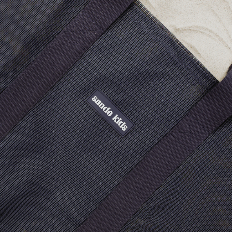Close-up of the high-quality features of the Sande Kids Beach Hauler mesh beach bag in Deep Sea Navy. Highlights the durable PVC mesh fabric, thick cotton straps, and silicone Sande Kids logo.