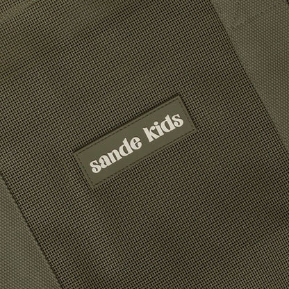 Close-up of the Sande Kids silicone logo on Pandanus Green PVC-coated mesh, featuring cotton strap detailing.