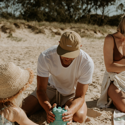 A lifestyle image of dad wearing the Sande™ cap while building sandcastles on the beach with his family.