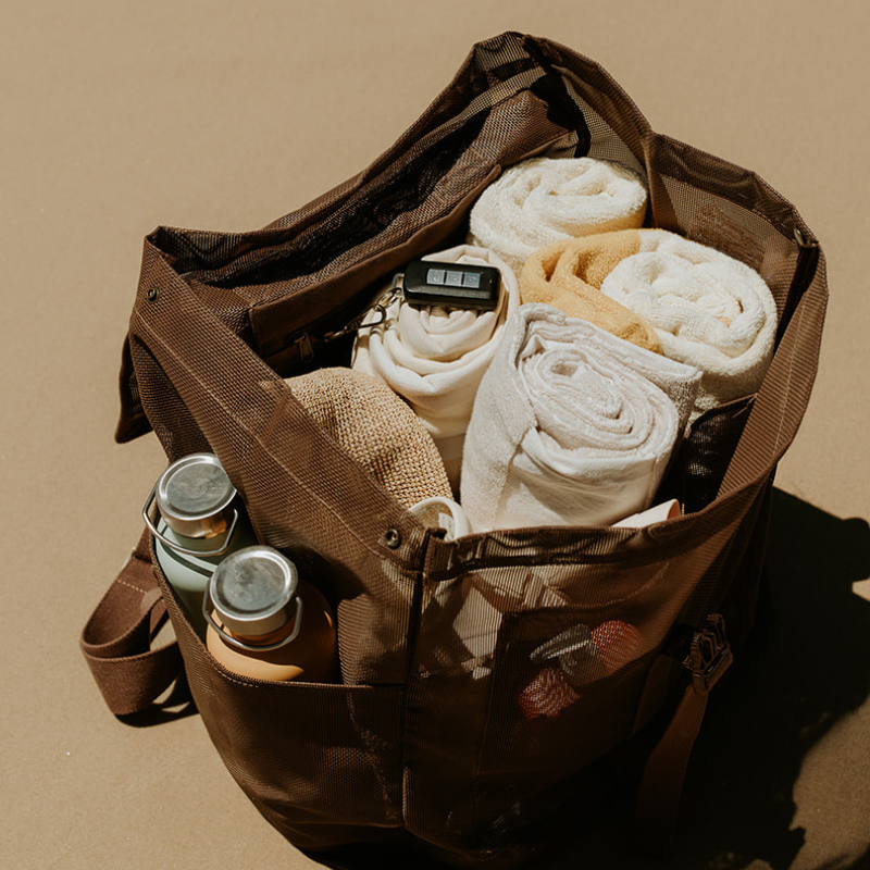 The Sande Beach Hauler Mesh Backpack in Espresso chocolate brown, fully packed with rolled towels and other beach essentials, demonstrating its spacious capacity and practical design.