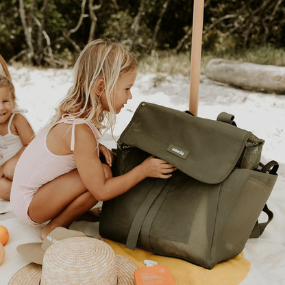 A lifestyle image of a young girl crouching next to the Sande Kids™ Beach Hauler mesh beach backpack in Pandanus Green. The spacious, sand-free mesh backpack features large side pockets for water bottles and toys, adjustable straps, and a durable construction. Ideal for family beach days, outdoor adventures, and carrying kids’ beach essentials while keeping sand out.