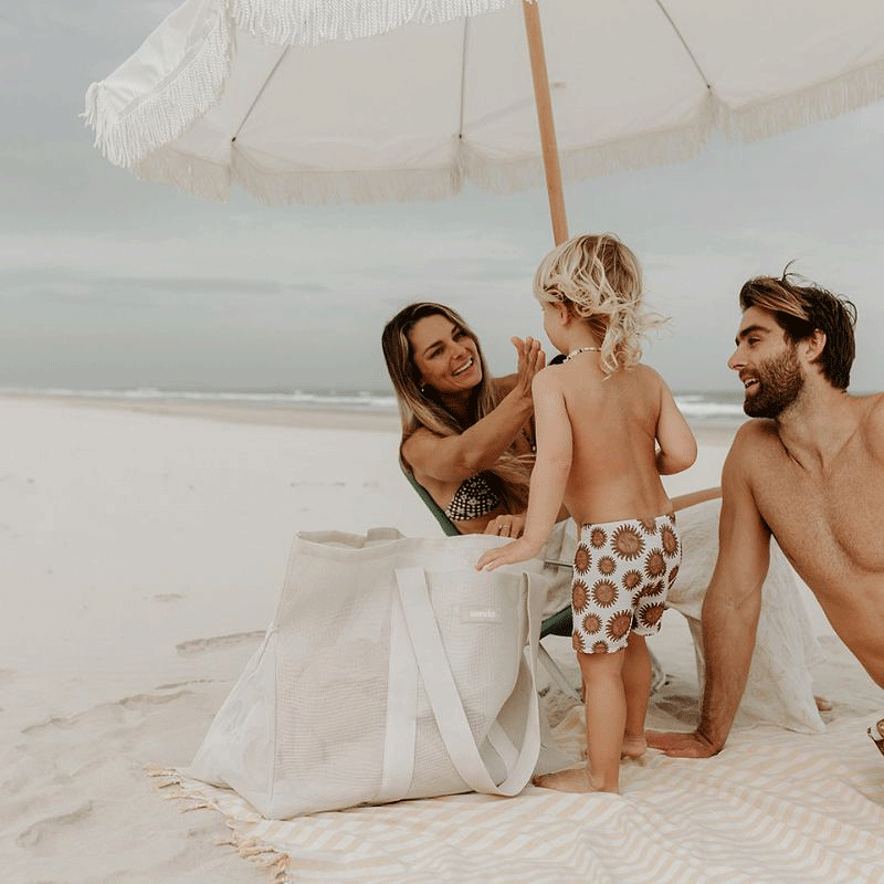 Family enjoying a day at the beach with their Sande Kids Beach Hauler oversized mesh beach bag in Sand, highlighting the bag&