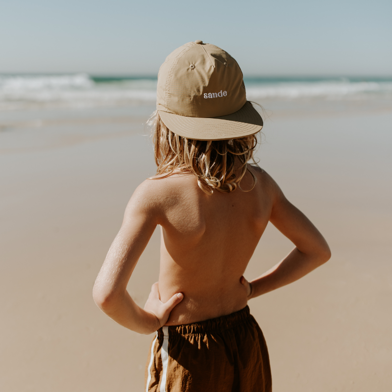 A little boy at the beach, with the ocean in the background, standing with his hands on his hips. He’s wearing the Sande™ cap on backwards, showcasing the embroidered Sande™ logo.
Cap is lightweight, fast-drying nylon. Perfect for outdoor adventures.